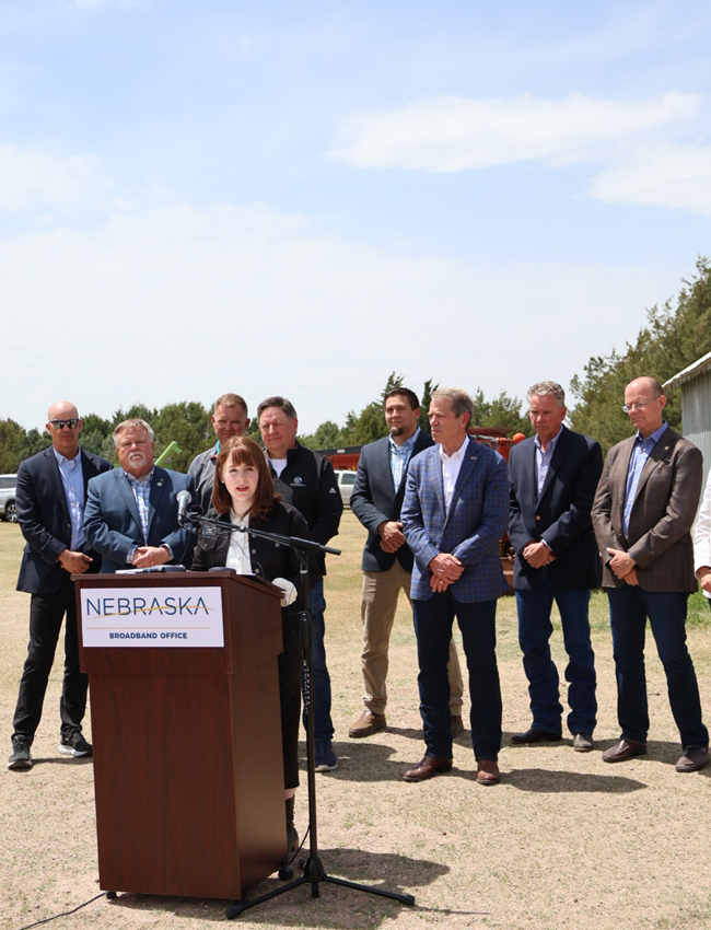 NTIA Administrator Arielle Roth delivering remarks at podium that says "Nebraska," surrounded by officials.